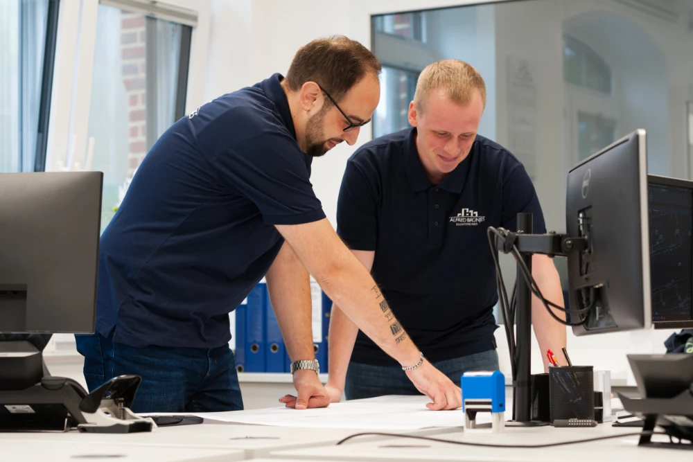 Zwei Personen, die zusammen auf einen Plan gucken, um so ein Projekt zu entwickeln.