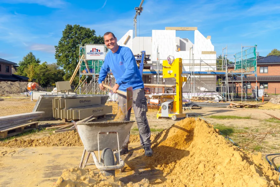 Ein Mitarbeiter schaufelt Sand von einem Haufen in eine Schubkarre.
