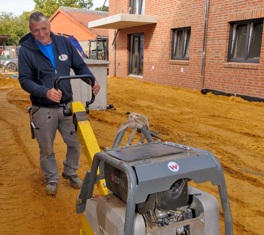 Ein Mitarbeiter plättet mit einer Rüttelplatte den Boden