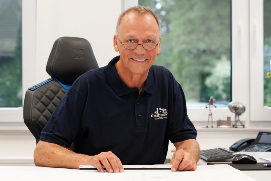 Ein Mitarbeiter der Firma sitzt am Schreibtisch und lächelt fröhlich in die Kamera.