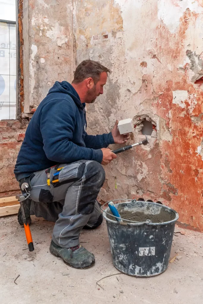 Ein Bauarbeiter hält einen Stein in der Hand, um damit ein Loch zu flicken.