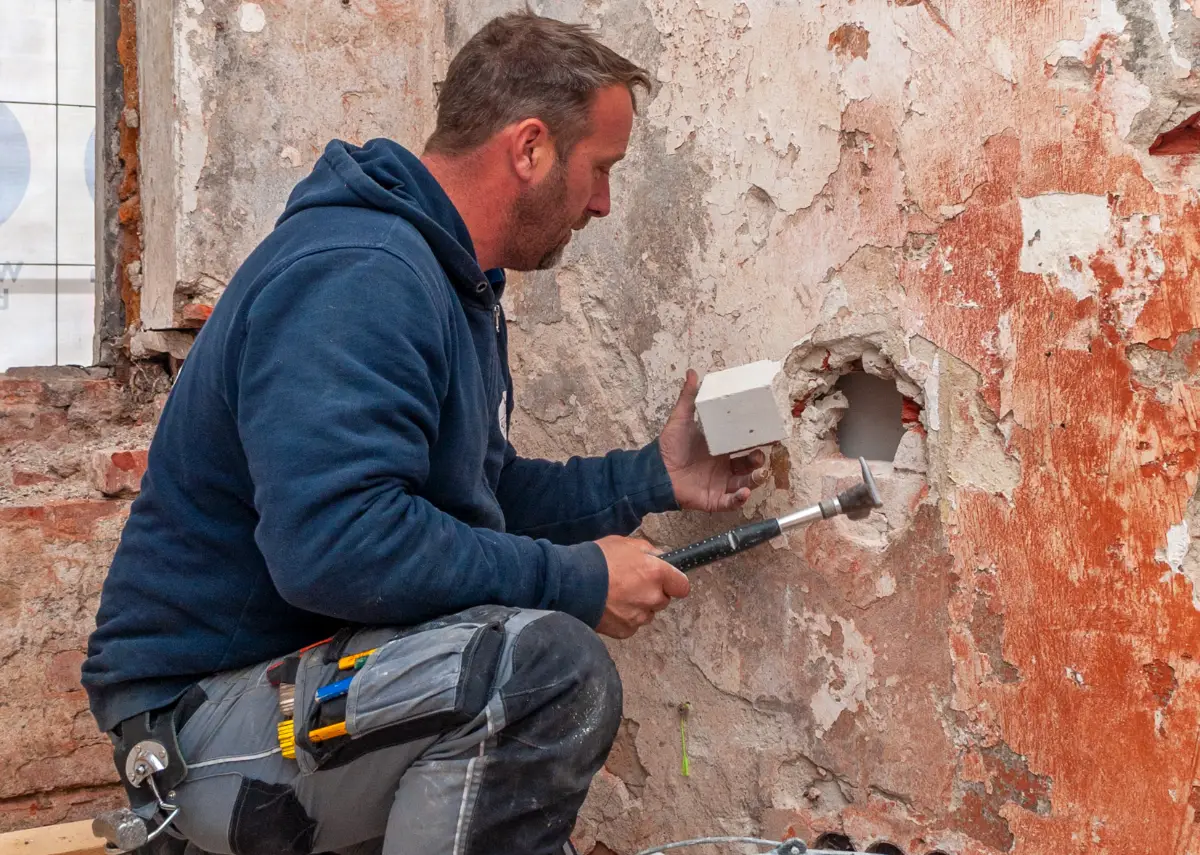 Ein Bauarbeiter hält einen Stein in der Hand, um damit ein Loch zu flicken.